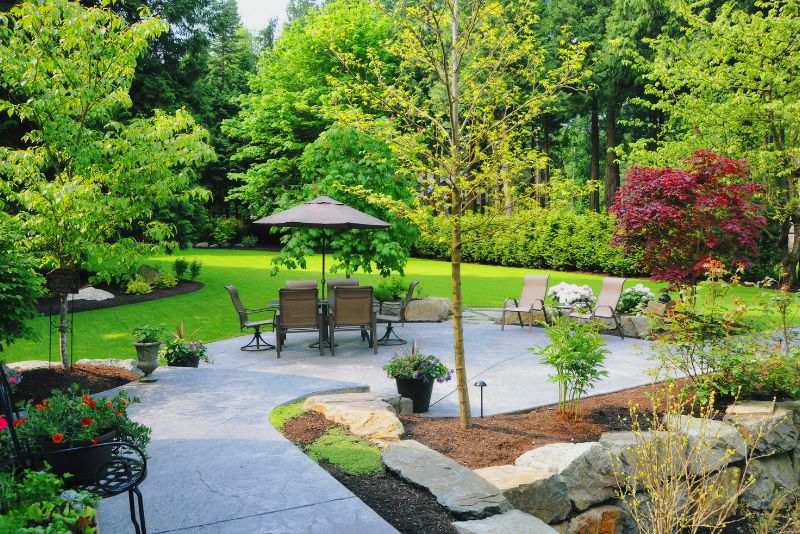 Landscaped backyard patio with garden beds, ornamental trees and outdoor dining furniture
